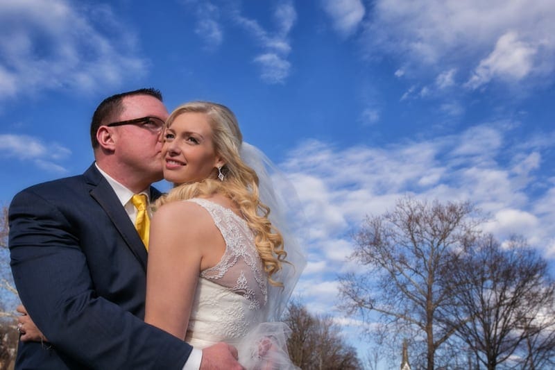 groom kissing brides cheek on bridge in chagrin falls