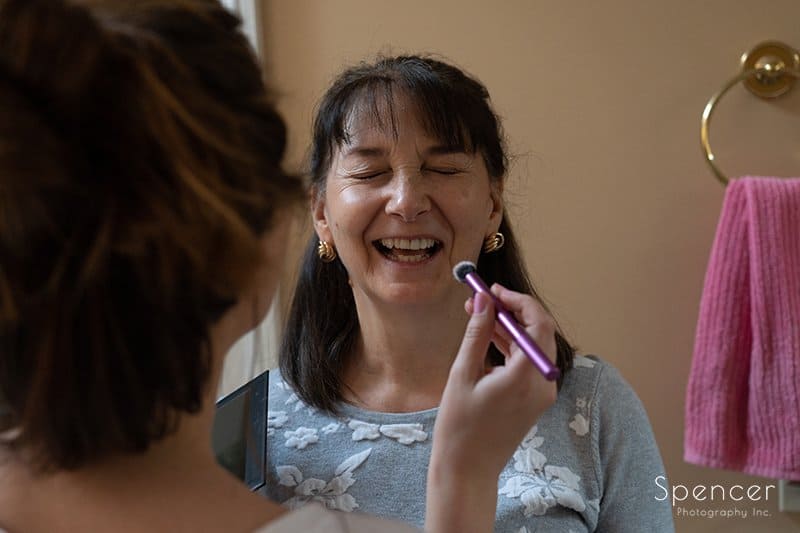 mom laughing as bride applies wedding day make-up